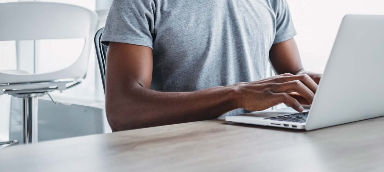 Young African American man sitting and using modern laptop in office
