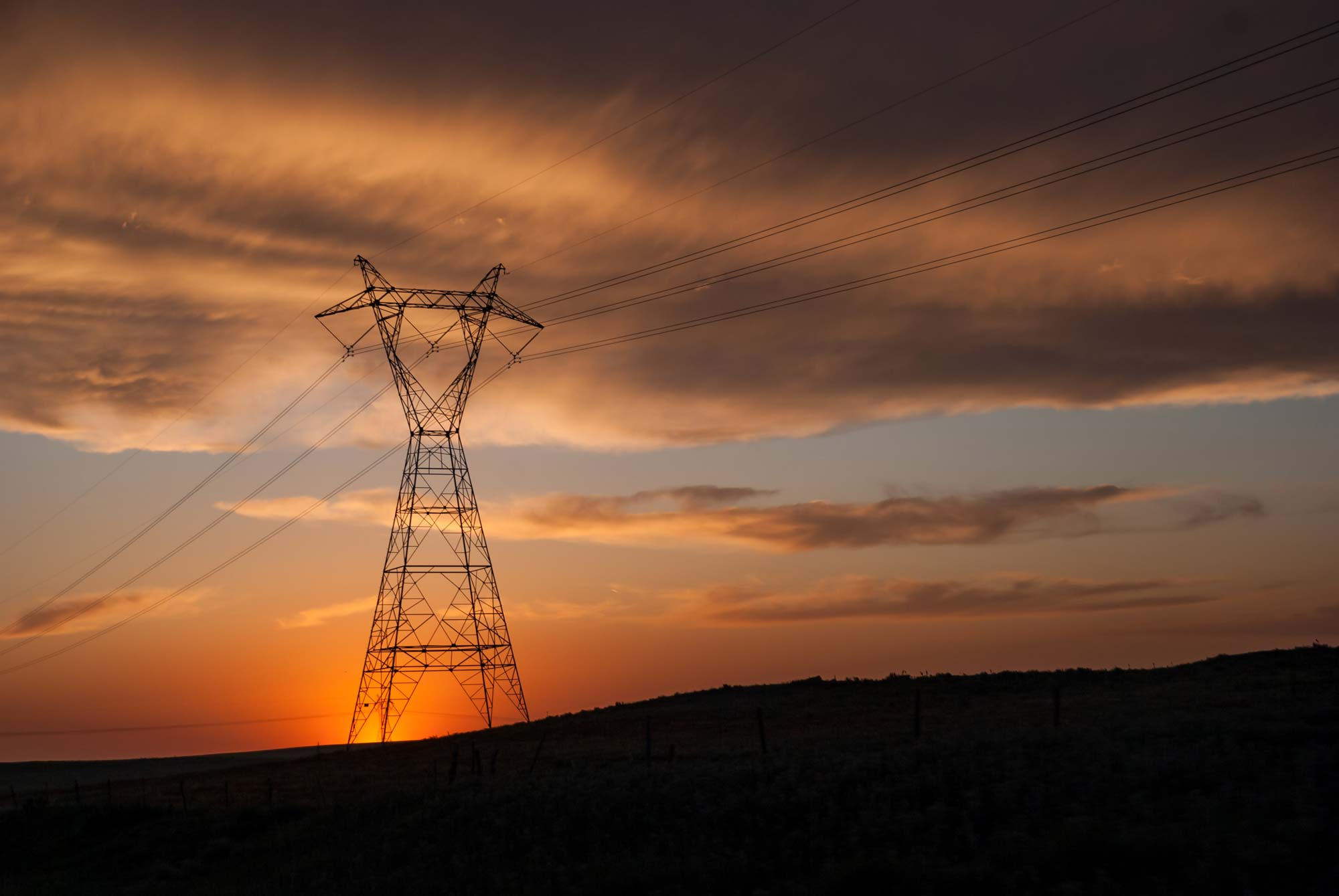 Power transmission tower in field at sunset