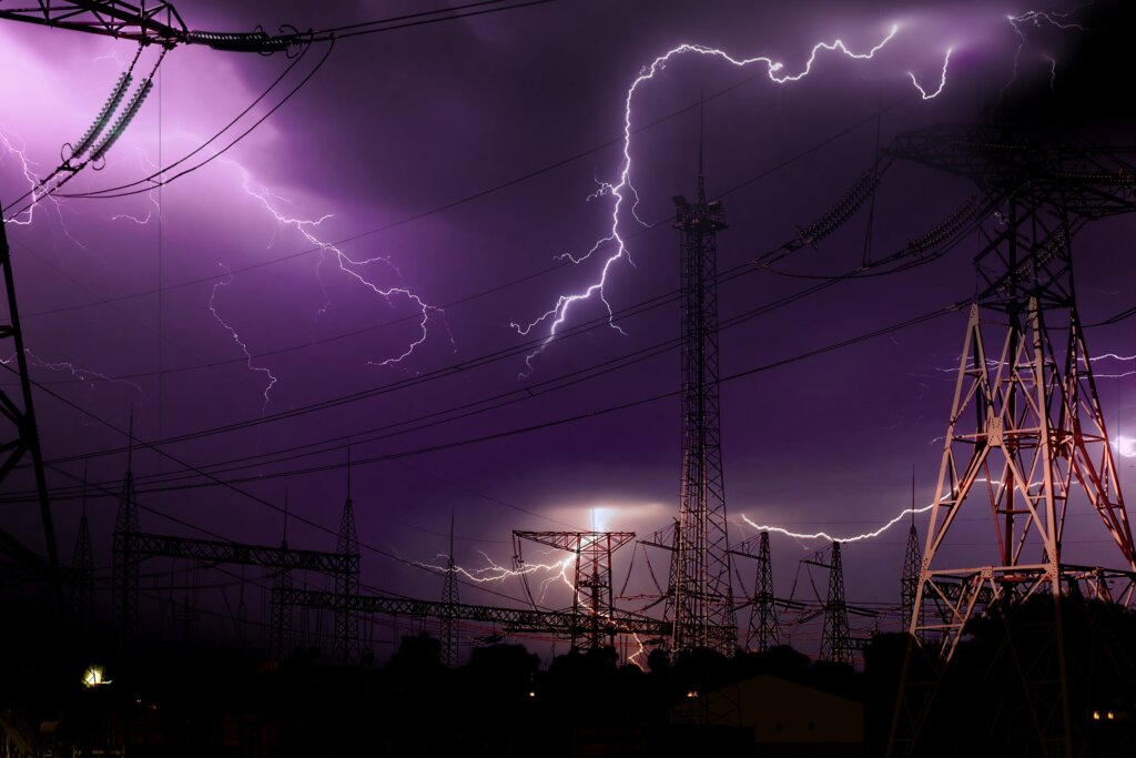 Ominous dark sky and lightning amidst transmission towers and power lines.
